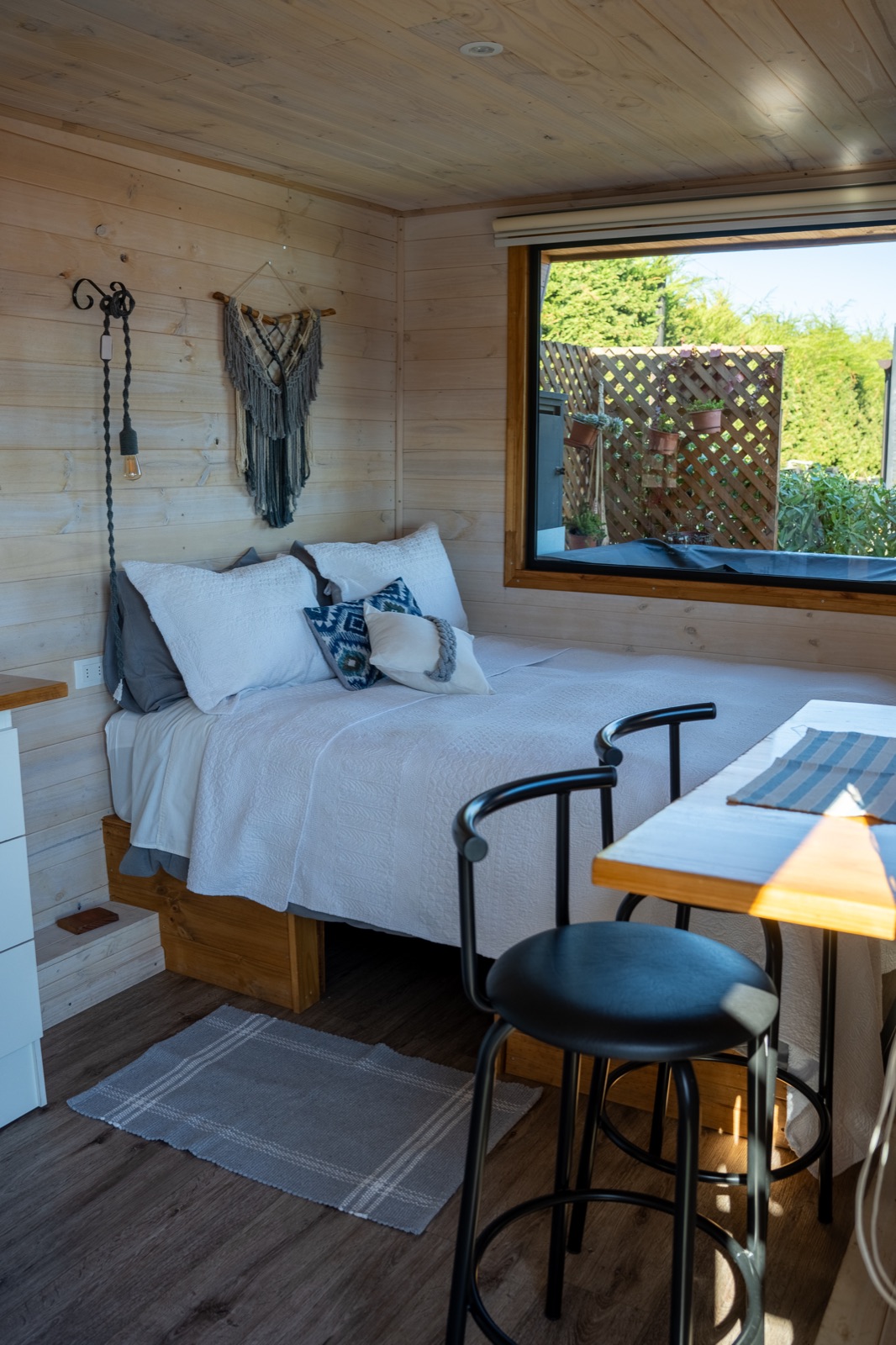 Cama de tiny house con detalles en macramé y mesa con vista
